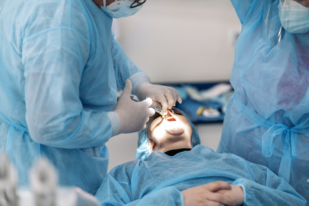 Male dentist wearing face mask and protective clothes doing treatment to unrecognized patient.